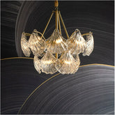 A close-up view of a gold chandelier with cascading frosted glass leaves against a dark, abstract background.
