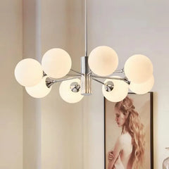 Side view of a polished chrome sputnik chandelier with frosted opal glass globes, with a framed artwork of a woman on the wall in the background.