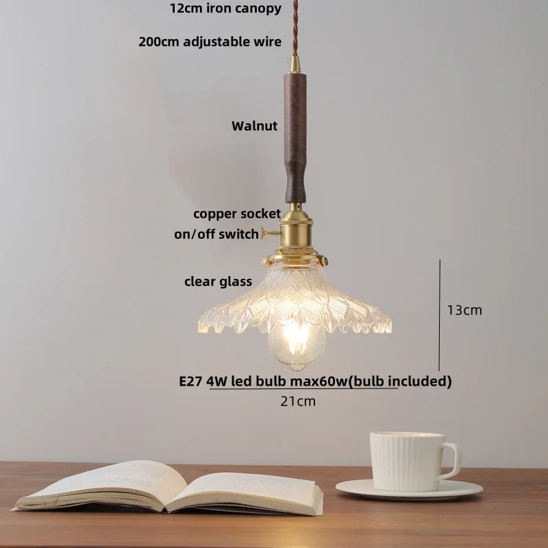 Pendant light with clear glass shade on a wooden table with an open book and a cup.