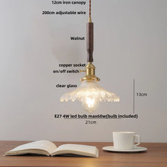 Pendant light with clear glass shade on a wooden table with an open book and a cup.