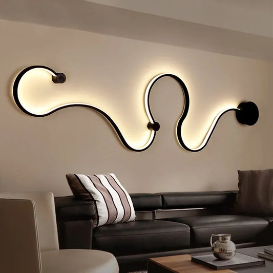 Black wave-shaped LED wall sconce with warm light mounted on a beige wall above a dark leather sofa.