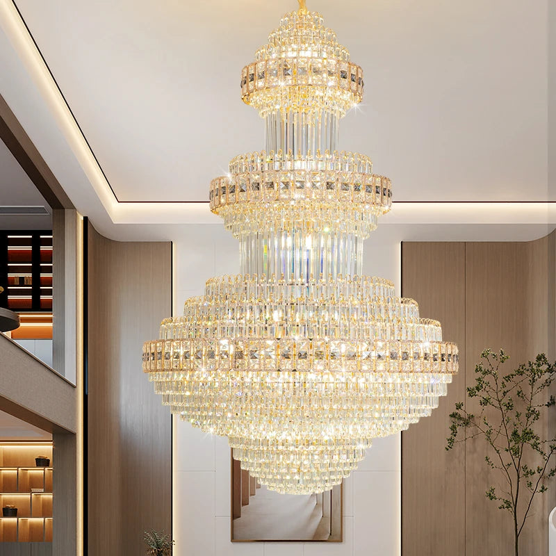 A grand gold crystal chandelier with multiple tiers, casting a warm glow in a spacious hall.