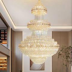 A grand gold crystal chandelier with multiple tiers, casting a warm glow in a spacious hall.