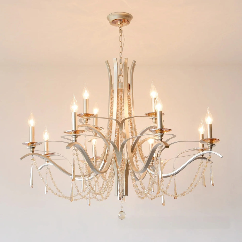 View of the brushed gold chandelier with illuminated candle-style bulbs and crystal accents against a neutral background.