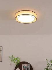 Close-up of a beige fabric drum flush mount ceiling light, with the light illuminated, casting a soft glow.