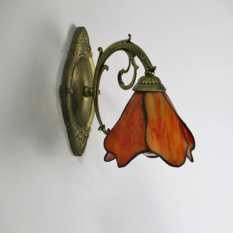 Decorative wall light fixture with orange glass shade and brass finish on a white background