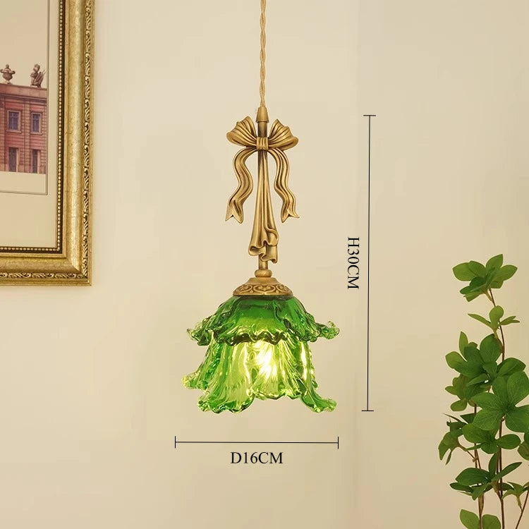 Green pendant lamp with gold fixture on a beige wall with plant and picture frame.