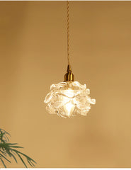 A single brass pendant light with a textured clear glass shade resembling a flower, against a warm background.