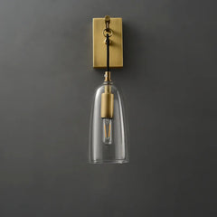 Close-up of a gold and clear glass bell wall sconce on a dark gray wall, showcasing the glass shade and bulb.
