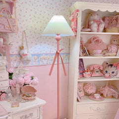 Close-up of a pink floor lamp with a pleated fabric shade and a pink bow, showcasing its decorative base.