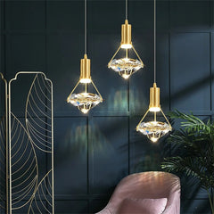 Three gold pendant lights hanging against a dark wall with a chair and plant in the foreground.