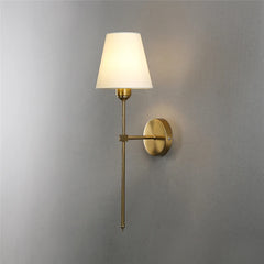 A brushed gold wall sconce with a white fabric shade illuminated against a grey wall.