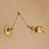 A brass swing arm wall sconce with a dome-shaped metal shade, mounted on a textured wall.