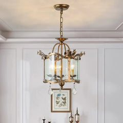 A gold chandelier with a distressed finish, glass cylinder shades, and crystal teardrop pendants hanging from a ceiling.