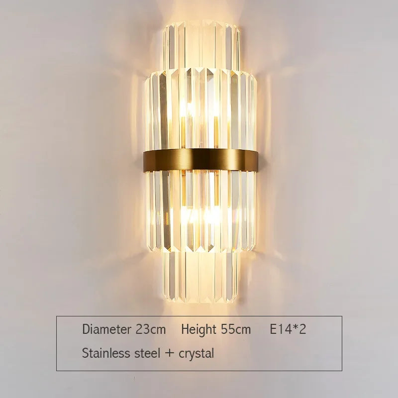Wall-mounted lamp with gold fixture and clear glass on a white wall, showing dimensions and material details.