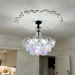 A multi-tiered glass chandelier with pearl accents suspended from a white ceiling with ornate molding.