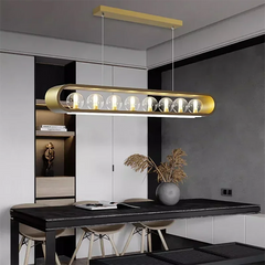 A contemporary gold pendant light with clear glass globes and an oval frame, installed over a dark wood dining table.