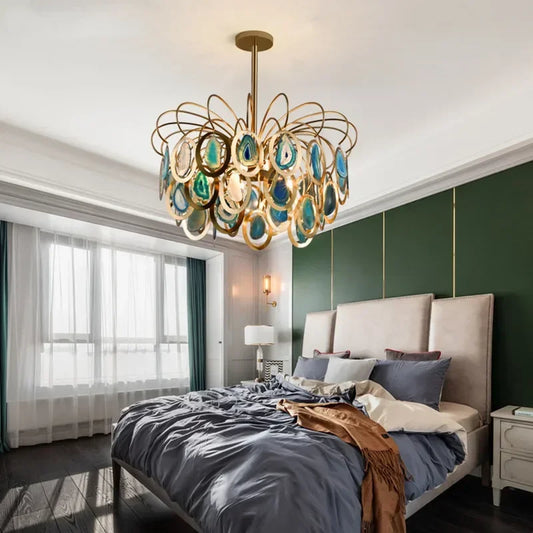 A gold chandelier with cascading agate slices hangs above a bed in a bedroom.