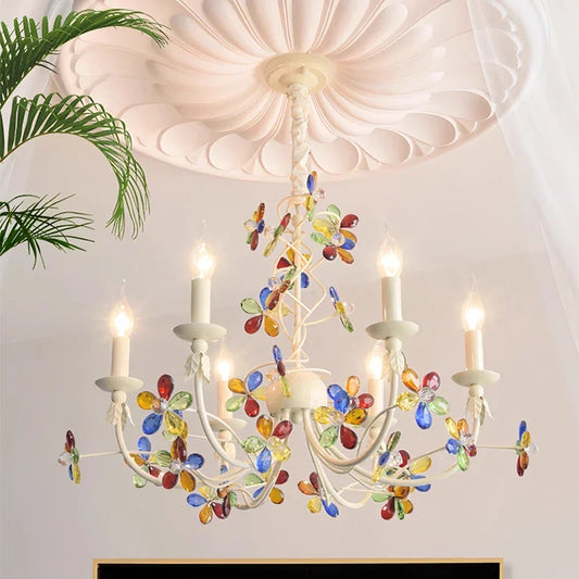Close-up of a white chandelier adorned with colorful crystal flowers and candle-shaped lights, mounted on a white ceiling with decorative molding.
