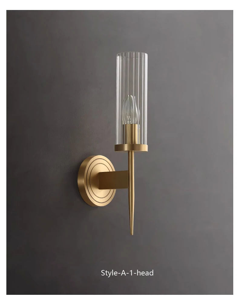 Gold wall sconce with clear glass shade on a dark gray background