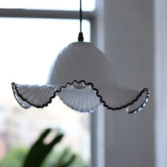 A white glass fluted pendant light with black trim hangs near a window with natural light, showcasing its shape.