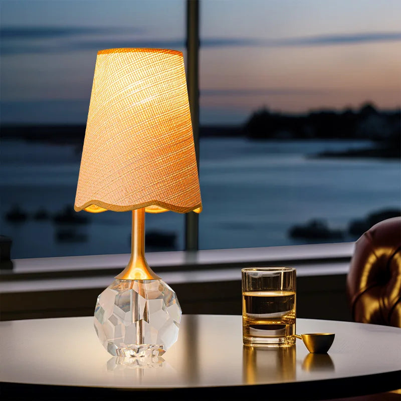 A gold and crystal table lamp on a round table by a window with a water view.