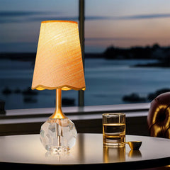 A gold and crystal table lamp on a round table by a window with a water view.