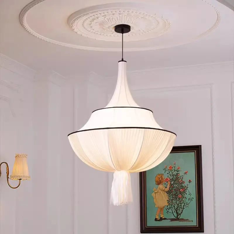 Close-up of a white fabric pleated pendant light with a black trim, hanging from a white ceiling with decorative molding, next to a framed picture.