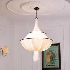 Close-up of a white fabric pleated pendant light with a black trim, hanging from a white ceiling with decorative molding, next to a framed picture.