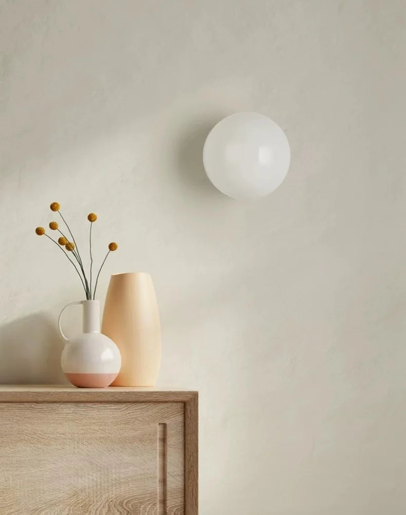 Wall-mounted spherical light fixture on a neutral wall with a wooden cabinet and vase.