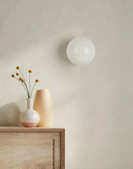 Wall-mounted spherical light fixture on a neutral wall with a wooden cabinet and vase.