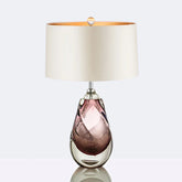 Purple glass swirl table lamp with a cream fabric shade reflecting on a surface