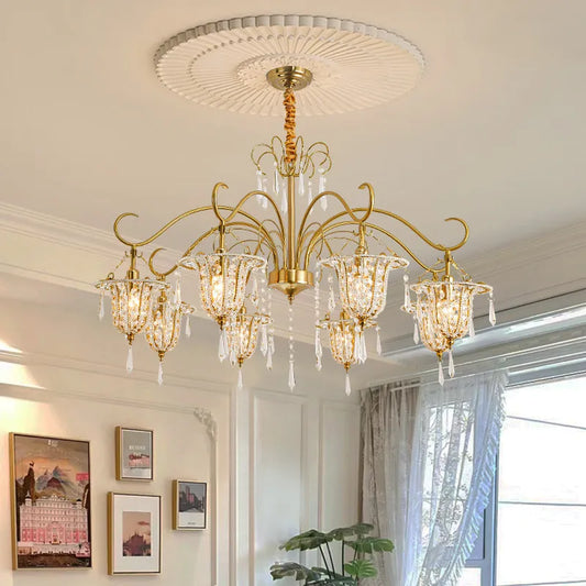 Gold crystal chandelier with floral-inspired arms and teardrop crystals, mounted on a white ceiling with decorative molding.