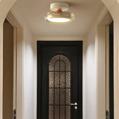 A contemporary flush mount ceiling light with a white base and a clear diffuser with a red accent, illuminating a hallway with a black arched door.