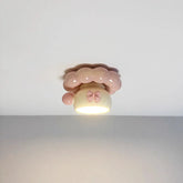 A pink ceramic coffee cup-shaped ceiling light with a pink bow and bubble-like trim, illuminated from below.
