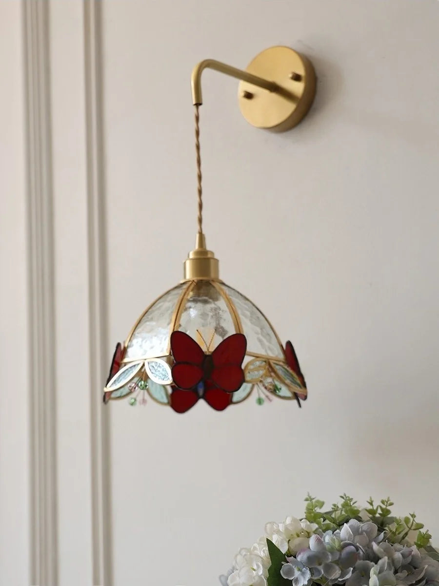 Wall-mounted lamp with stained glass shade featuring butterfly design on a light-colored wall.