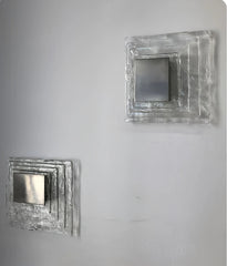 Two square metallic wall art pieces on a gray background
