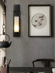 Wall-mounted light fixture and framed artwork on a gray wall with a teapot and cups in the foreground.