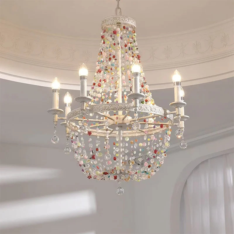 Close-up of a white multi-arm chandelier adorned with colorful beads and crystal drops, illuminated.