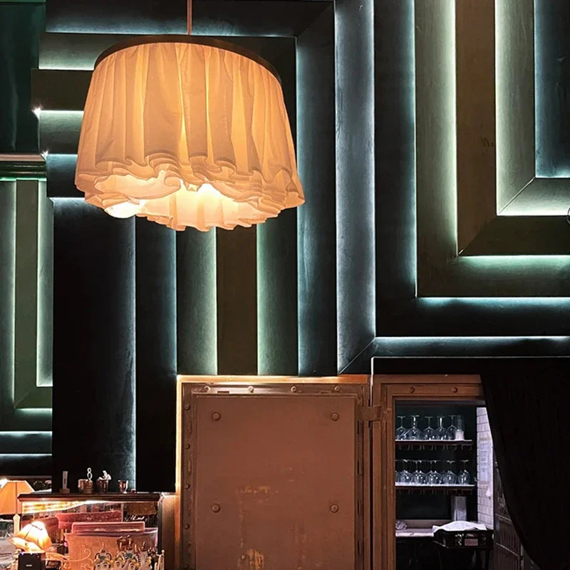A white fabric ruffled pendant light illuminated against a dark, geometrically patterned wall with LED accent lighting.
