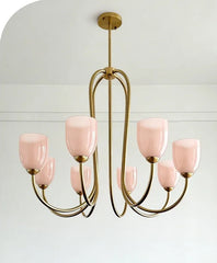Brushed gold chandelier with pink tulip glass shades hanging against a white background.
