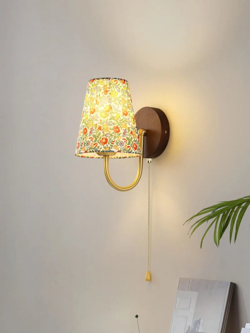 Wall-mounted lamp with floral-patterned shade on a plain wall.