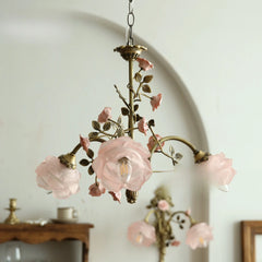 Close-up of a brass chandelier with pink rose bud accents and frosted glass shades.