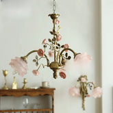 A brass chandelier adorned with pink rose buds and ceramic flowers, hanging against a white wall.