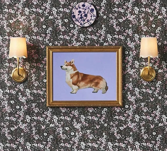 Floral-patterned wall with framed picture of a dog, two floral chairs, and wall sconces.