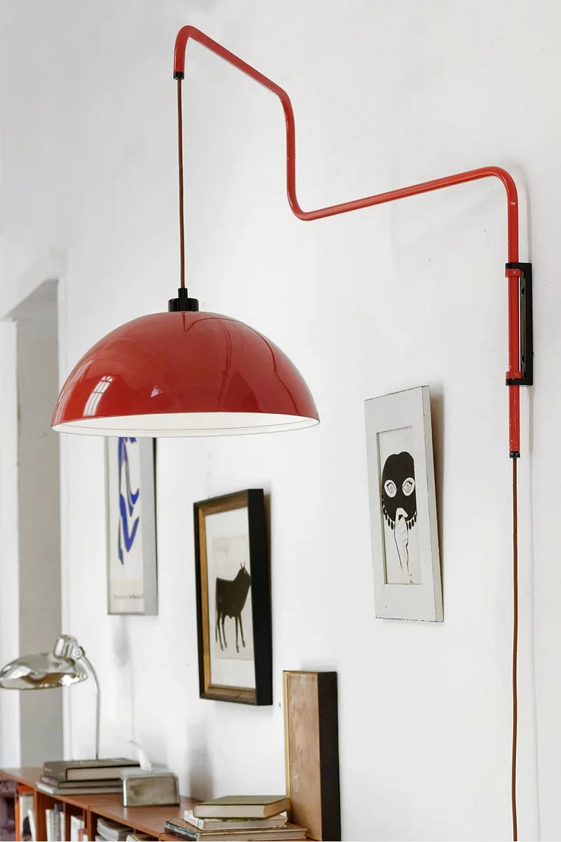 Red pendant lamp with a long arm in a room with framed pictures on the wall.