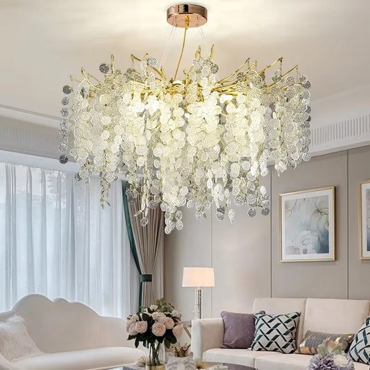 Gold cascading crystal pendant light fixture in a modern living room with white sofas and sheer curtains.