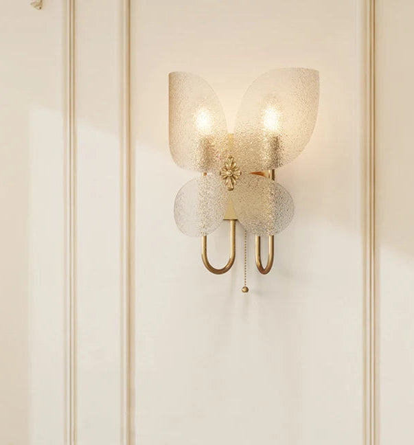 Close-up of the gold butterfly wall sconce, highlighting the textured frosted glass wings and central floral accent.