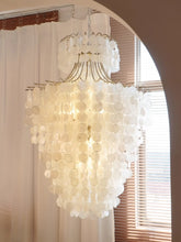 A large, tiered chandelier with many circular capiz shell discs hanging from a gold-colored frame, illuminated from within.