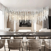 Curved chandelier with numerous clear crystal teardrops hanging from dark branches, suspended over a dining table.